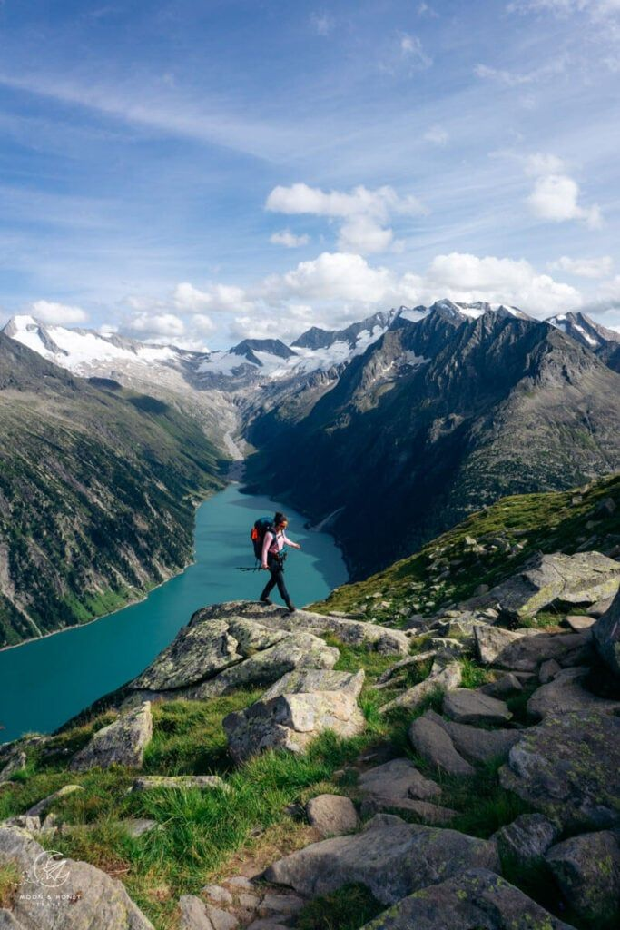 Hiking in the Austrian Alps: a mountain trail through alpine meadows with dramatic snow-capped peaks in the background