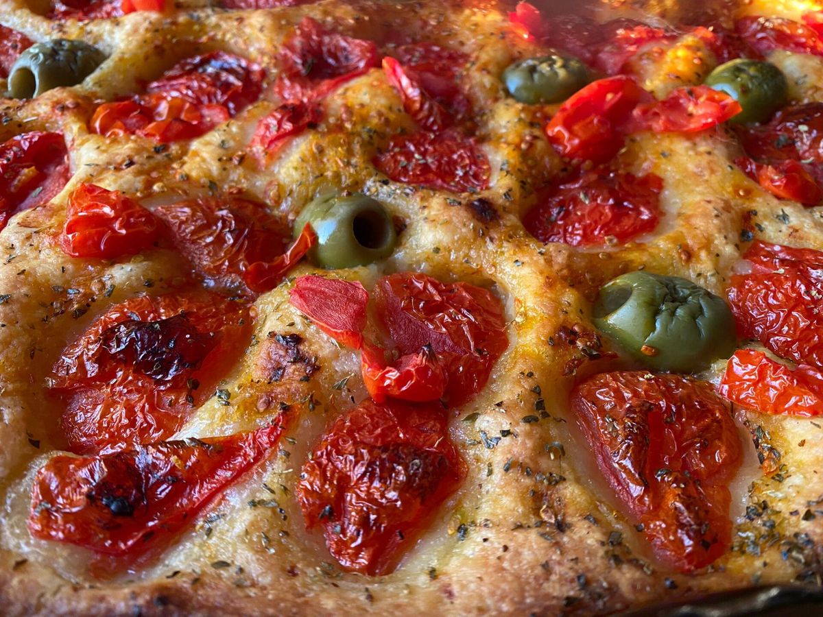 A golden focaccia barese topped with cherry tomatoes, olives and oregano, fresh from the oven