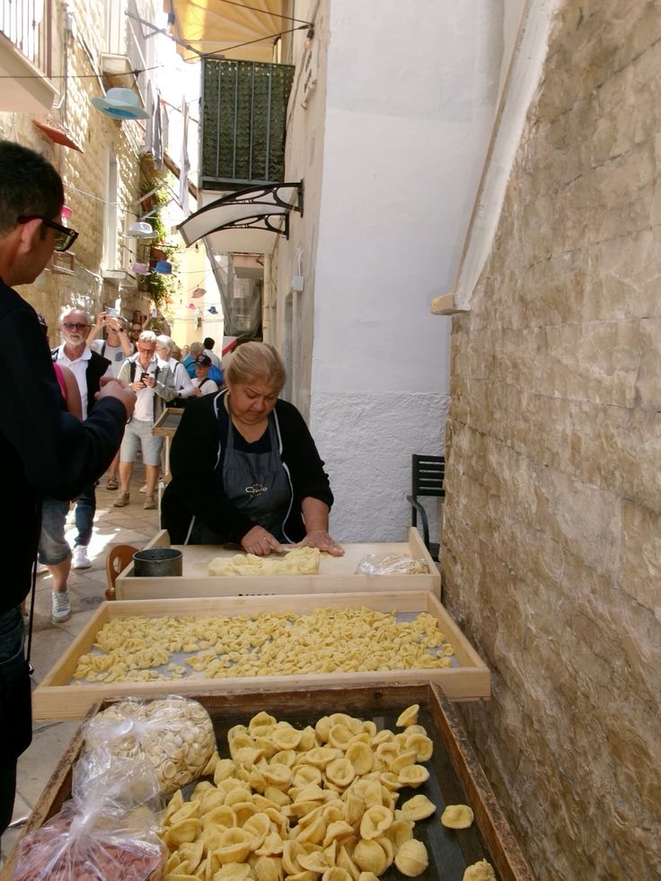 Fresh handmade orecchiette pasta drying on a wooden board in a sunlit alleyway of Bari Vecchia