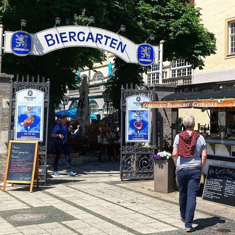 A traditional Bavarian beer garden in Munich under the shade of old chestnut trees, with long wooden tables filled with locals enjoying Hefeweizen and pretzels