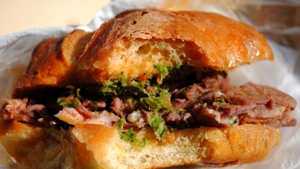 A traditional lampredotto sandwich, Florentine street food, served on a soft roll with green sauce and chilli