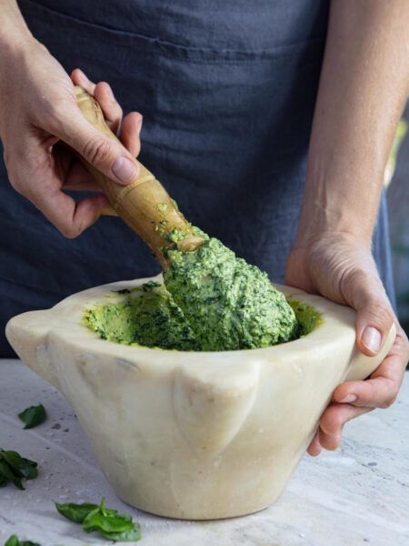 Traditional Genoese pesto being prepared in a marble mortar with a wooden pestle, the authentic way