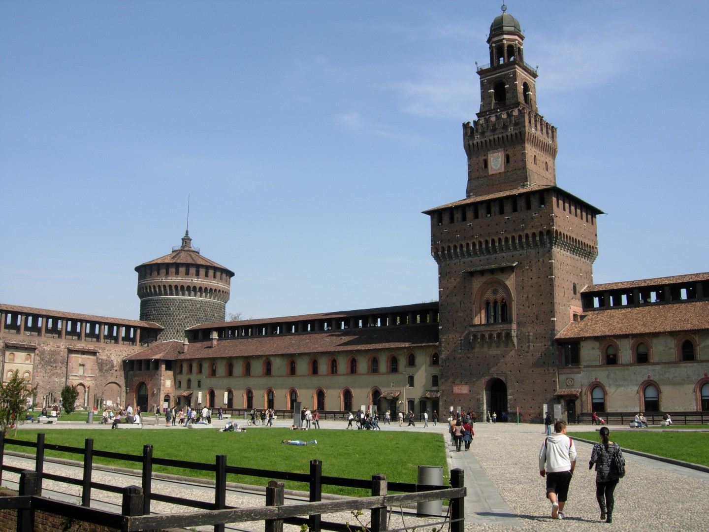 The imposing red brick facade of Sforza Castle in Milan, with its central tower and surrounding moat.