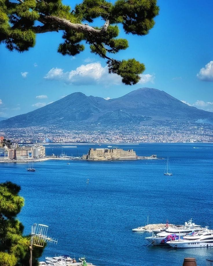 Mount Vesuvius rising above the Gulf of Naples, seen from the Posillipo coast in the late afternoon light, with the city of Naples spread between the volcano and the sea
