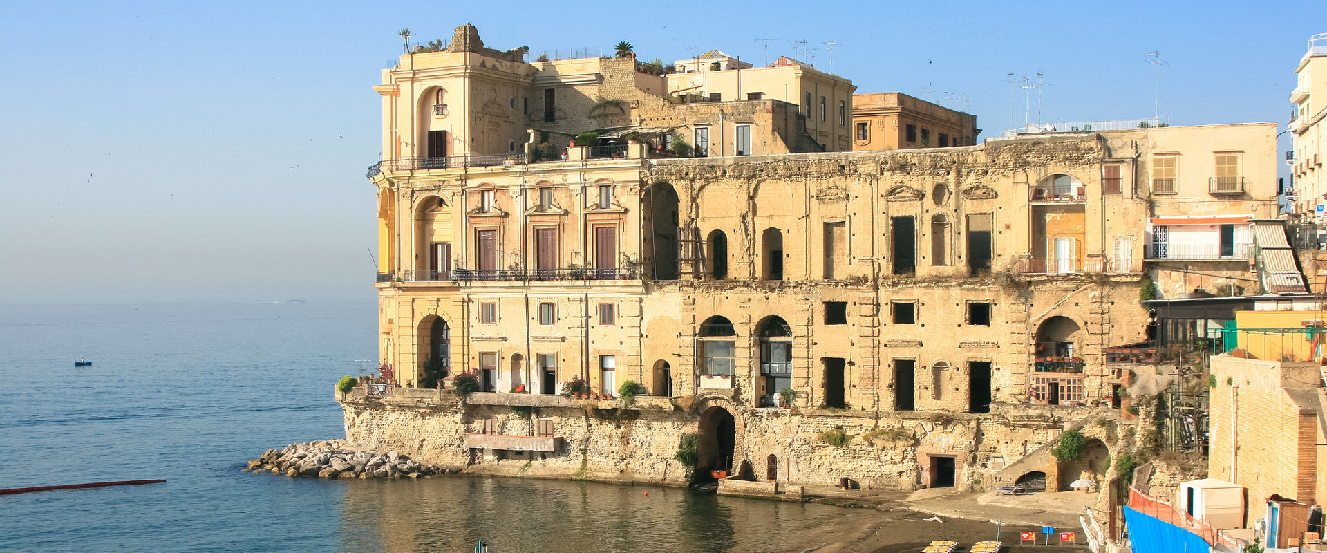 The Palazzo Donna Anna rising from the rocks of the Posillipo coast above the Gulf of Naples, its unfinished baroque facade worn by centuries of sea air and legend