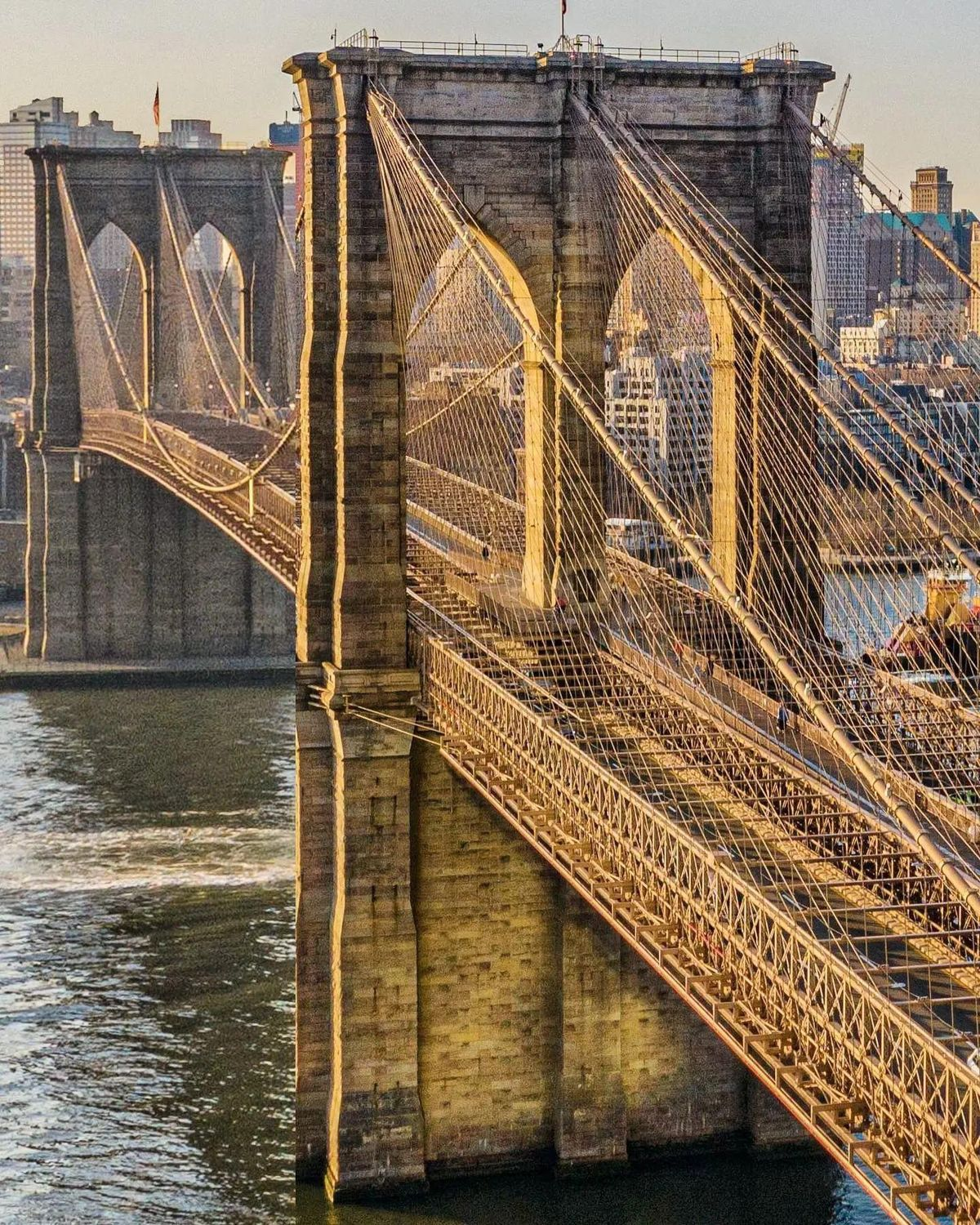 The Gothic stone towers of the Brooklyn Bridge illuminated against a twilight sky, with the Manhattan skyline in the background.