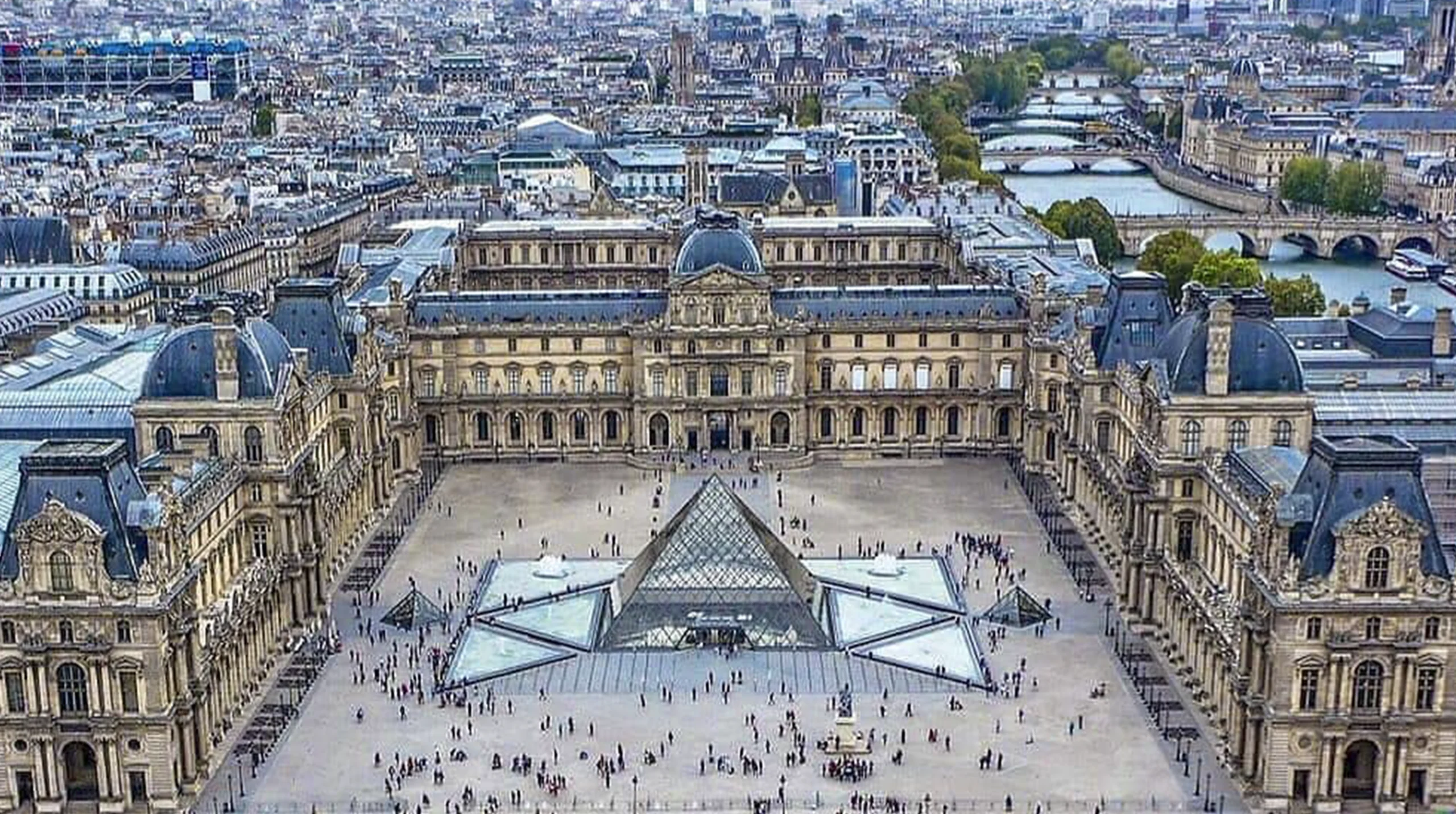 The glass pyramid of the Louvre Museum at twilight, with the historic palace facade illuminated behind it.