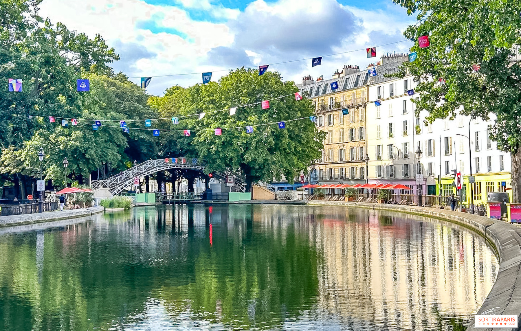 The picturesque Canal Saint-Martin lined with trees and bridges, with people sitting along the quays.