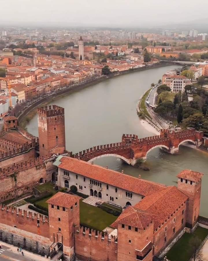 The Adige River winding through Verona at sunset, with the cathedral and Castel San Pietro in the background.